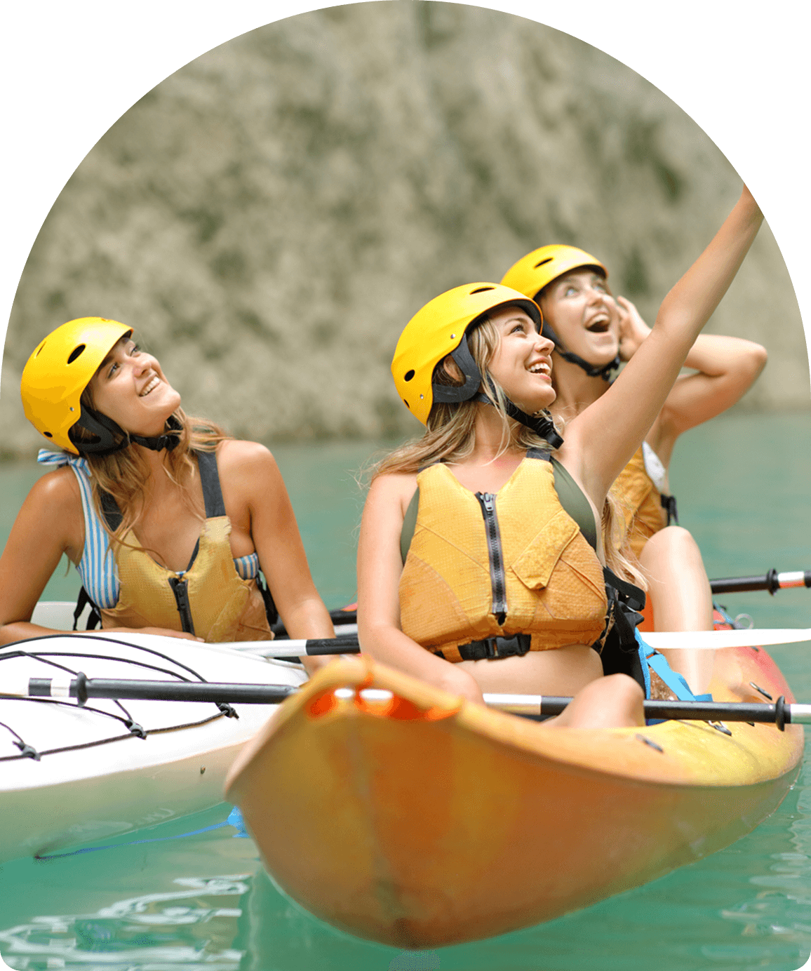 Three women kayaking, wearing helmets, smiling.